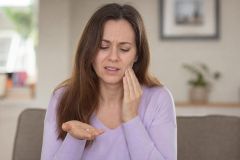 Woman at home holding a lost dental filling, touching cheek from tooth pain.