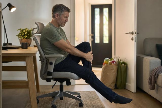 Middle-aged man at home holding his knee, appearing in pain and contemplative.
