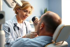 Doctor examines patient with otoscope in a clinic. Medical professional performs checkup, showing healthcare and wellness focus. Bright, clean environment, white coat, diagnostic tool.