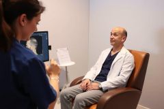 Doctor examining a patient's X-ray in a medical office. A healthcare professional reviews an image while the patient sits comfortably. Clinical setting, diagnostic imaging, healthcare.