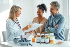 Doctor consulting with a couple about health supplements and nutrition. Bright, modern office setting with blueberries, vitamins, and a medical chart. Focus on wellness, healthcare, and preventative medicine.