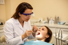 Dentist in a clinical operatory inspects a patient's open mouth with a mirror and probe.