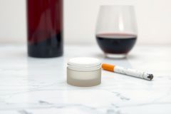 Close-up of a small jar, cigarette, and glass of red wine on a marble surface. Focus on textures and details. Soft lighting. Lifestyle image.