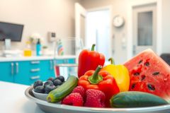 Fresh fruits and vegetables arranged on a silver platter. Includes watermelon, blueberries, raspberries, cucumbers, and bell peppers, set against a blue kitchen backdrop. A healthy and vibrant food arrangement.