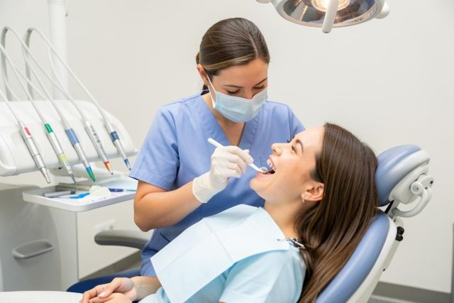 Dental hygienist in mask brushing a teenage patient's teeth with braces during a routine dental checkup.