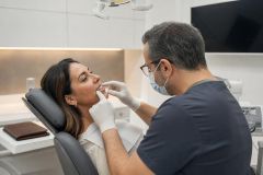 Dental patient receiving oral exam from masked dentist in modern clinic, discussing veneers/care.