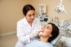Dentist compares a veneer shade tab to a smiling patient's teeth in a dental exam chair.