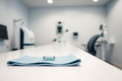 Modern ophthalmology clinic interior. Blue drape covers a lens on a white examination table. Blurred background includes diagnostic equipment, suggesting eye care and vision testing. Cool, neutral color palette with a focus on cleanliness and medical technology.