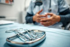 Surgical instruments on a blue medical tray in a clinic setting. A doctor in scrubs is blurred in the background. Focus on stainless steel tools, healthcare, and medical equipment. Blue and silver tones.