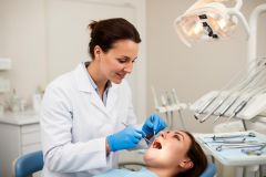 Dentist wearing gloves examining a patient's open mouth with a dental mirror and probe in a clinic.