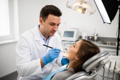 Dentist examining a patient's teeth with a dental mirror while patient reclines in a modern clinic chair.