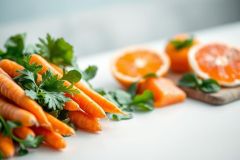 Fresh carrots and citrus fruits, including oranges and grapefruits, are displayed on a white surface. Vibrant orange hues dominate the image, accented by green parsley, suggesting healthy eating and fresh produce. A bright, clean aesthetic.