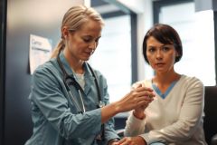 Doctor examines a patient's wrist, wearing a white coat and stethoscope. Healthcare setting, medical checkup, patient care, blue and white tones.