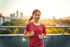 The image depicts a woman standing on an outdoor balcony or ledge during the golden hour. She is wearing athletic attire, including a red top, with her hair tied back. 