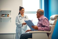 Doctor consults with a patient in a medical office. A female doctor in a white coat is reviewing a chart with an elderly man. Healthcare, examination, and patient care are visible.