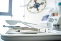 Medical instruments and a vial on a stainless steel tray. Laboratory setting with equipment visible in the background. Sterile environment, likely a hospital or research lab. White and silver tones dominate the image.