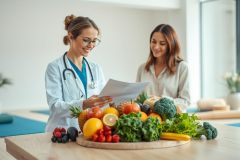 Doctor and patient discussing nutrition plan with fresh fruits and vegetables on a table. Bright, healthy food, medical consultation, wellness, and dietary advice are key themes. Focus on healthy lifestyle and preventative care.