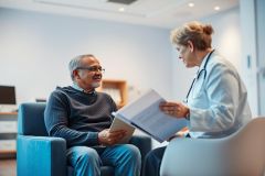 Doctor consults with a senior patient in a modern, brightly lit clinic. The image depicts healthcare, medical consultation, and elderly care, featuring a female doctor reviewing documents with a male patient. Blue and neutral tones dominate the scene.
