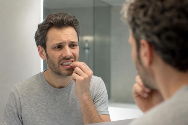 Man examining irritated gums in a bathroom mirror, concerned about teeth whitening side effects.