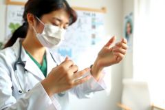 Healthcare worker in scrubs and mask performs hand hygiene. Close-up view showing proper handwashing technique in a medical setting. Focus on cleanliness and safety.