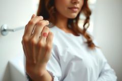 Close-up of a woman's hand with neatly manicured nails, likely in a bathroom setting. Soft lighting and a neutral color palette create a serene and clean aesthetic. Focus on nail care and beauty.