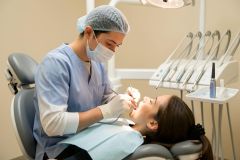 Dentist in mask and gloves performing a dental procedure on a reclined patient in clinic.