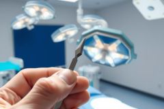 Surgical instruments in a brightly lit operating room. A scalpel is held in hand, showcasing medical tools and a sterile environment. Focus on precision and healthcare.
