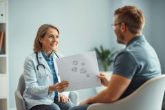 Doctor discussing medical scan results with a patient in a bright, modern office. A female physician wearing a stethoscope reviews an X-ray with a male patient, promoting healthcare and medical consultation. Blue and white tones create a calming atmosphere.