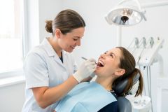 Dental hygienist carefully examines a smiling patient's open mouth in a bright, modern dental clinic.