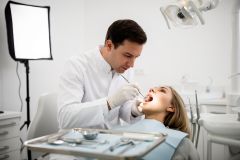 Dentist examining a patient's open mouth and gums in a bright dental operatory, assessing oral health.