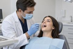 Dentist examining a patient's teeth in a bright dental clinic, patient reclined with bib.