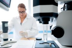 Scientist in lab coat using a microscope for research. Close-up view of the lab environment with equipment and glassware. Focus on scientific analysis and discovery.