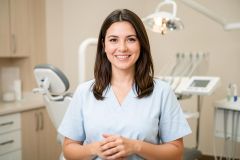 Smiling dental hygienist in a treatment room, showing natural-looking teeth and welcoming patient care.
