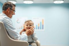 Doctor examining a baby during a pediatric checkup. Warm, inviting blue clinic setting with charts in the background. Focus on healthcare, child wellness, and gentle medical care. Smiling faces convey trust and comfort.