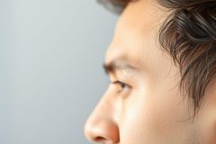 Close-up portrait of a person's face in profile. Focus on eye and nose. Natural lighting. Simple background. Minimalist portrait photography.