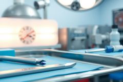 Surgical instruments on a stainless steel tray in an operating room. Blue sterile drapes and medical tools are visible, suggesting a surgical procedure. The scene conveys a clinical and sterile environment.