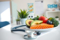 Healthy salmon and avocado plate with broccoli and blueberries. A nutritious meal arranged on a white plate with a blue stethoscope in the background. Focus on wellness and balanced diet.