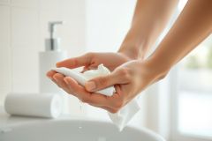 Close-up of hands holding a white towel in a bathroom setting. Clean, bright, and minimalist aesthetic. Focus on hygiene and personal care.