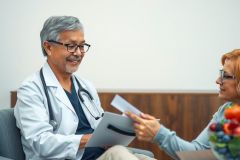 Doctor and patient during consultation. Male physician in white coat reviews paperwork with a female patient in a healthcare setting. Focus on medical exam, doctor-patient interaction, and healthcare services.