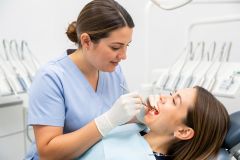 Dental hygienist examining a patient's gums with a mirror and probe during a periodontal check.