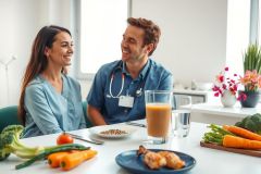 A healthcare worker in scrubs enjoys a healthy breakfast with vegetables and fruit at a kitchen table. The scene evokes wellness and a balanced lifestyle.