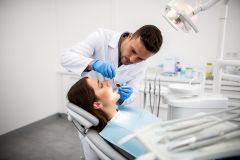 Dentist inspects a patient's open mouth with a mirror and probe in a bright clinic chair to check healing.