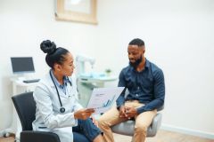 Doctor discussing medical chart with patient in a clinic. Healthcare professional reviewing data, patient consultation, medical examination, office setting, blue scrubs, beige pants.