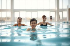 Three children swimming in a bright, indoor swimming pool. The scene features blue water, large windows, and a modern architectural setting. A fun, active moment of kids enjoying a pool day.