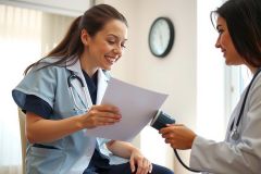 Doctor examining a patient in a clinical setting. The doctor is wearing a stethoscope and reviewing paperwork while the patient sits comfortably. Healthcare, medical checkup, consultation, doctor patient relationship.
