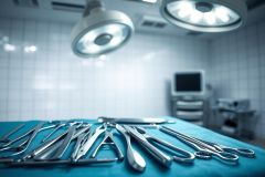 Surgical instruments laid out on a blue operating table in a sterile operating room. Bright surgical lights illuminate stainless steel tools against a blurred background with medical equipment. Focus on medical tools, healthcare, and surgical setting. Cool blue and silver tones dominate the scene.