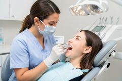 Dental hygienist in mask examining patient's teeth with mirror and probe during a routine checkup.