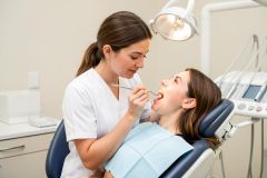 Dental clinician performs an oral exam with a mirror while a patient reclines in a dental chair.
