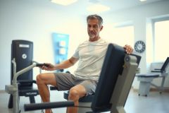 Man exercising on a seated leg press machine in a bright gym. He's wearing athletic clothing, showcasing a fitness and workout scene. Focus on strength training and healthy lifestyle.
