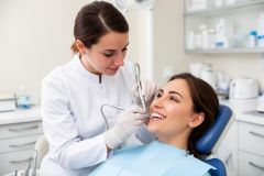 Young woman reclining in a dental chair, smiling as a dentist in gloves performs a routine cleaning with handpieces.